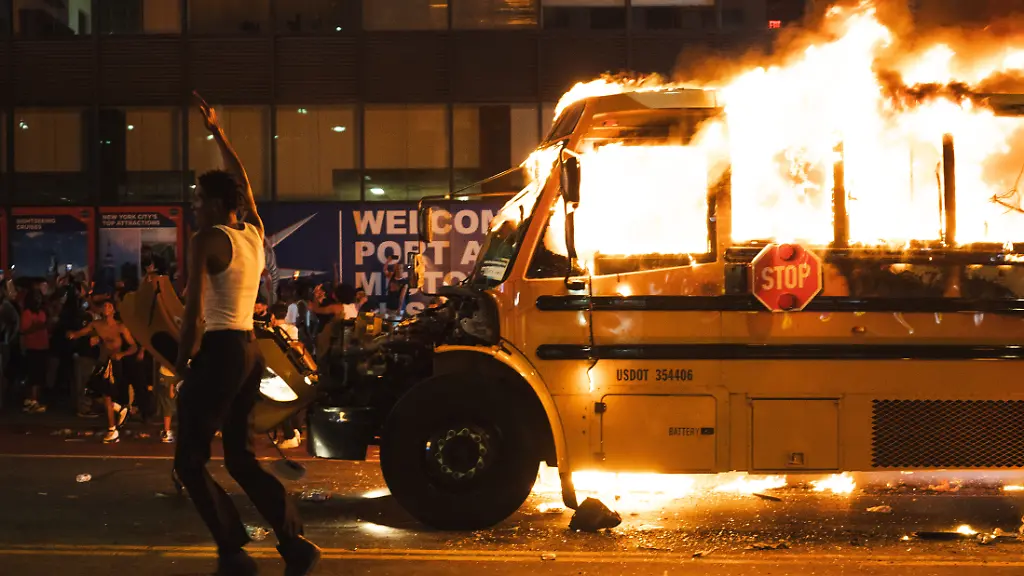 June-14-2026-New-York-New-York-USA-A-man-with-a-white-shirt-on-jumps-in-the-air-with-his-hand-raised-as-he-runs-past-a-yellow-school-bus-that-was-lit-ablaze-during-the-celebration-of-the-New-York-Knicks-winning-the-NBA-Finals
