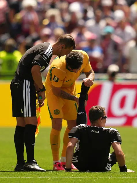 Fussball-Maenner-WM-2026-USA-Australien-Vorrunde-Gruppe-D-Spieltag-2-Seattle-Stadion-Schiedsrichter-Felix-Zwayer-Deutschland-sitzt-auf-dem-Rasen-bekommt-vom-Australier-Aiden-O-Neill-Unterstuetzung