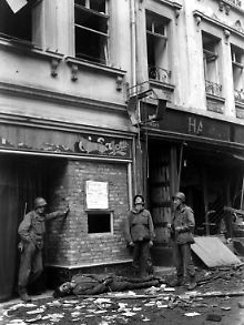 Drei US-Soldaten im April 1945 in Aschaffenburg. Neben ihnen liegt ein Wehrmachtssoldat, der in den letzten Kriegstagen aufgehängt worden war. Die GIs haben den Deutschen abgeschnitten.