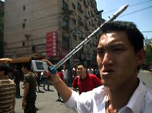 Ein mit Mobiltelefon und Stahlrohr bewaffneter Chinese in Ürümqi.