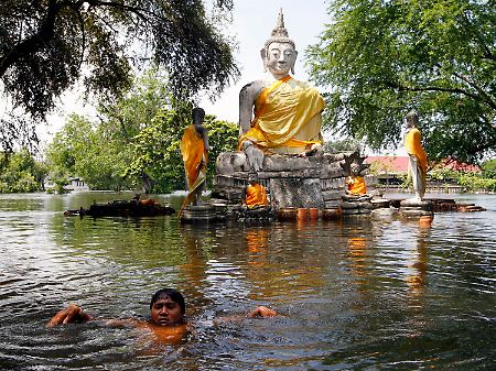 Eine Buddhastatue in der Tempelanlage von Ayutthaya steht im Wasser.