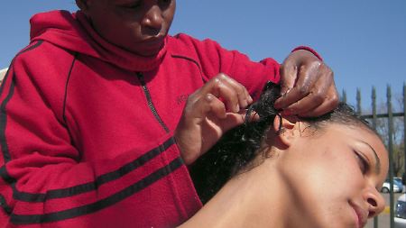 Eine Kundin lässt sich von Friseurin Nomsa Mncube am Rand einer Straße in Johannesburg "Braids" flechten. 