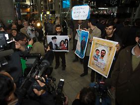 Auf dem Flughafen von Teheran demonstrieren junge Männer mit Bildern des iranischen Führers Chamenei und des Atomwissenschaftlers Mostafa Ahmadi Roshan, der am 11. Januar in Teheran bei einer Explosion getötet wurde.