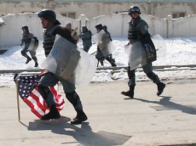 Sicherheitskräfte tragen eine amerikanische Flagge weg, die der wütende Mob angezündet hat.