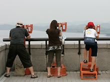 Besucher eines Aussichtspunkts blicken von Südkorea auf ein nordkoreanisches Dorf.