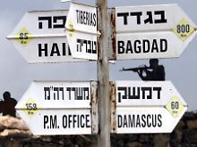 Wegweiser zeigen auf dem Mount Bental auf den Golanhöhen verschiedene Richtungen an, u. a. in Syriens Hauptstadt Damaskus. Im Hintergrund: Soldaten aus Pappmaché.