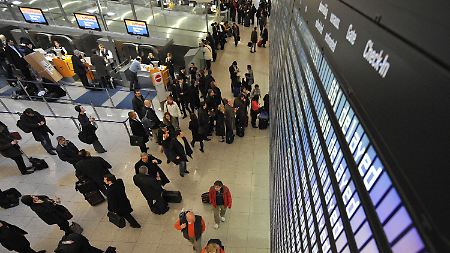 Passagier stehen am Flughafen München unter einer Anzeigetafel. Zahlreiche Flüge sind verspätet.