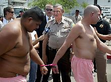Joe Arpaio (M) wird interviewt, während Gefangene in rosa Unterwäsche an ihm vorbeiziehen müssen.