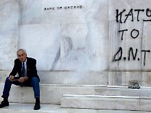 Ein Mann sitzt vor der "Bank of Greece". Das Graffiti fordert: "IWF raus".