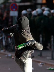 Ein Vermummter wirft eine Flasche auf Polizisten.