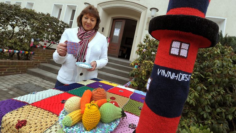 Petra Schulz präsentiert ihr bestricktes Kaffeegeschirr zusammen mit bestrickten Steinpfeilern, Gemüse und einem Leuchtturm.