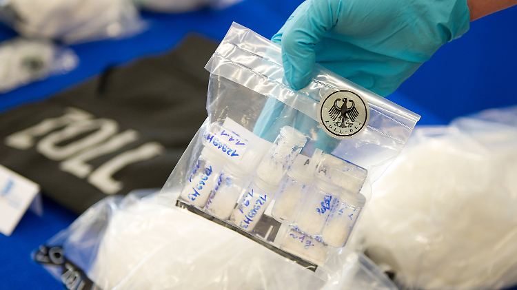 Vor einem Tisch auf dem sich 20 Kilogramm Crystal befinden, hält ein Zollbeamter eine Tüte Drogentests in den Händen.