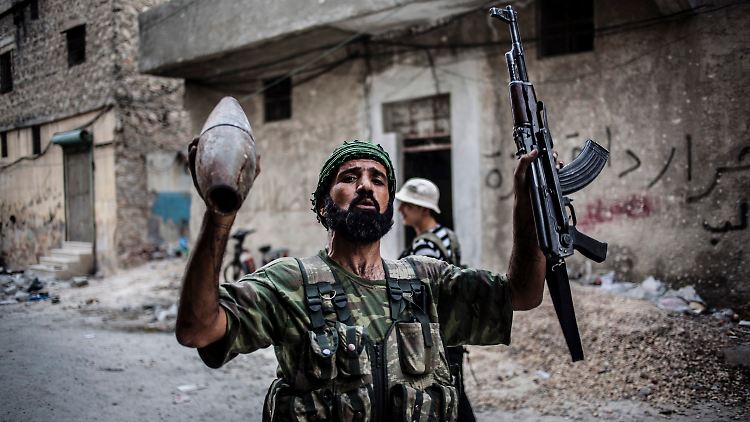 Ein Kämpfer der Freien Syrischen Armee hält seine Maschinenpistole und ein abgefeuertes Artilleriegeschoss der Regierungstruppen in den Händen. 