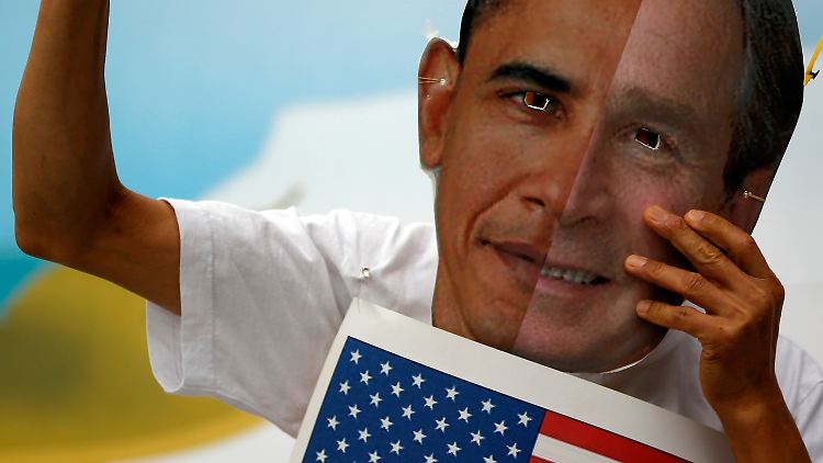 Ein Anti-Kriegs-Aktivist demonstriert mit Masken von US-Präsident Obama und Ex-Präsident Bush.