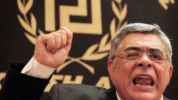 Nikolaos Michaloliakos, der Chef der Goldenen Morgenröte. Auf der Fahne im Hintergrund ist das an ein Hakenkreuz erinnernde Parteisymbol zu sehen.