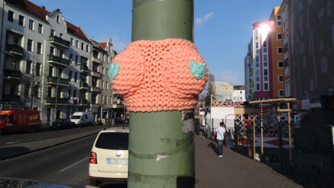 Eine besondere Form der Streetart ist das Guerilla oder Urban Knitting: Dabei werden Bäume, Fahrräder oder Pfeiler mit Stricksachen umgeben. Oder ein Mast bekommt einen schicken BH verpasst, wie hier von Emmanuelle Esther in Berlin-Neukölln.