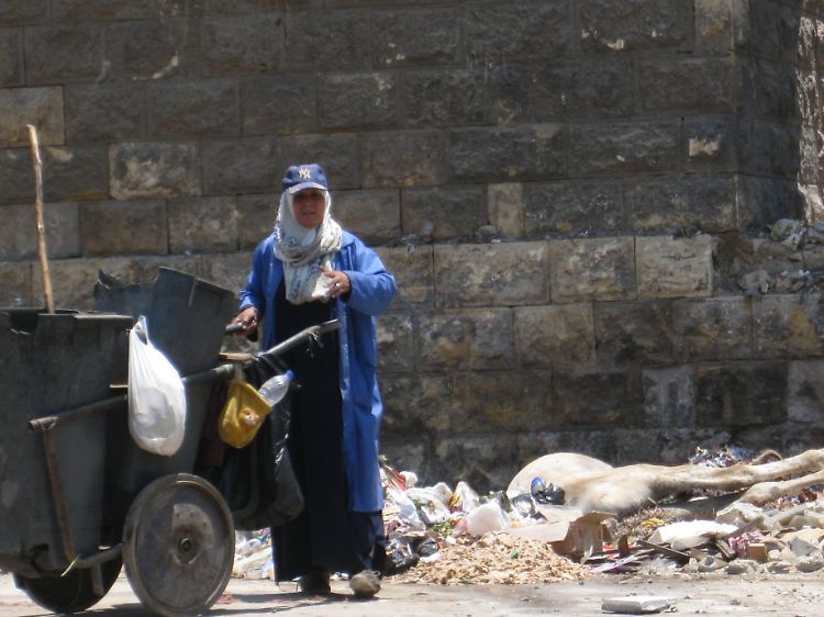 Eine Straßenkehrerin steht am Aquädukt im Viertel Magra al-Ojun neben einem Müllhaufen, auf dem auch ein totes Pferd liegt.