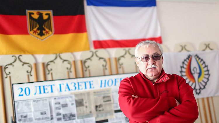 Juri Gempel posiert in seinem Büro vor der deutschen und der Krim-Flagge.