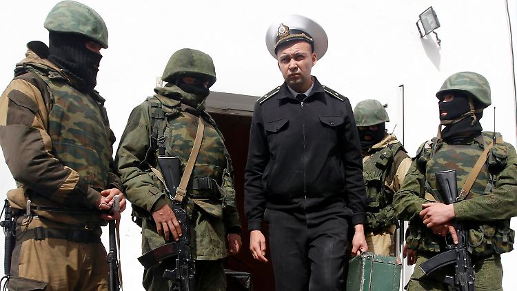 Ein ukrainischer Offzier verlässt die Marinebasis in Sewastopol. Vermummte Soldaten ohne Abzeichen überwachen den Abzug.