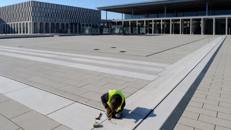 Ein Handwerker arbeitet an den Bodenplatten vor der Kulisse des neuen Hauptstadtflughafens.