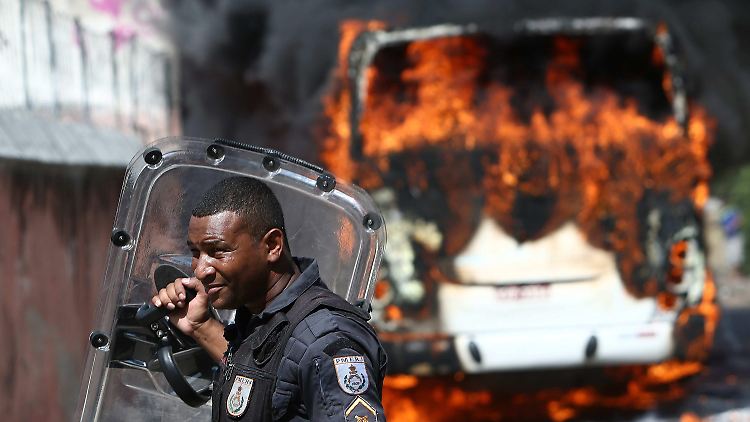 Ein Polizist vor einem brennenden Bus in Rio.