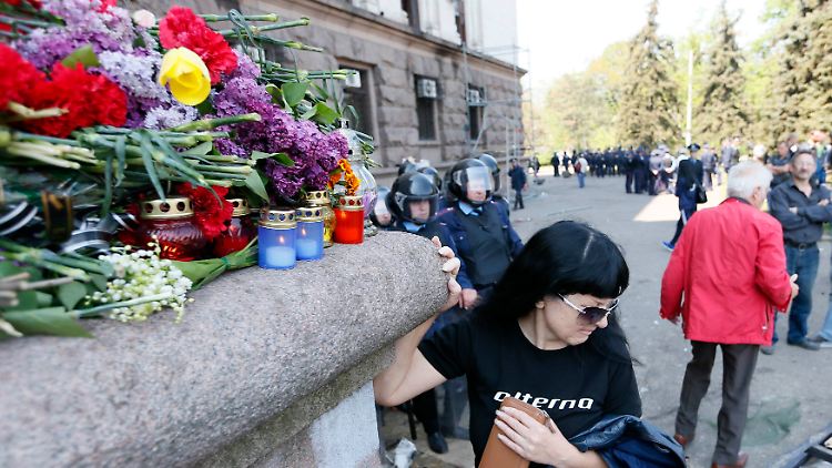 Blumen liegen vor dem ausgebrannten Gebäude in Odessa, eine Frau wendet sich trauernd ab.
