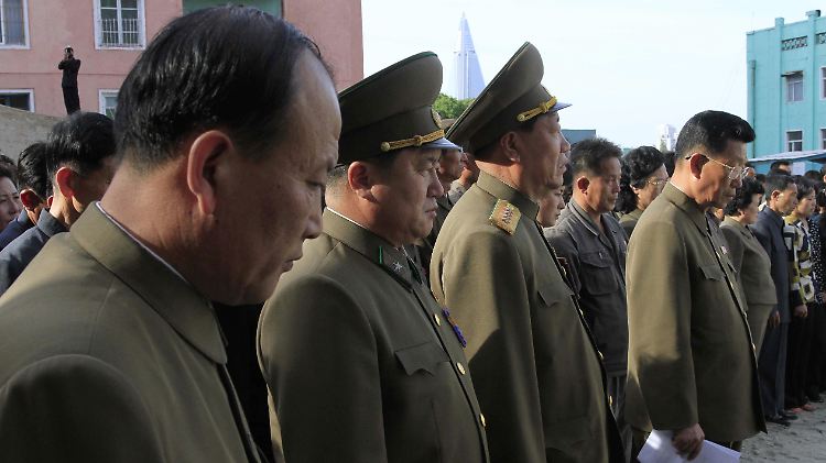 Nordkoreanische Staatsbedienstete und Offiziere stehen mit Angehörigen der Opfer an dem Unglücksort.