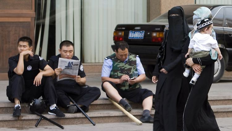 Ürümqi Juli 2009: Frauen der ethnischen Minderheit der Uiguren laufen an chinesischen Sicherheitsbeamten vorbei.