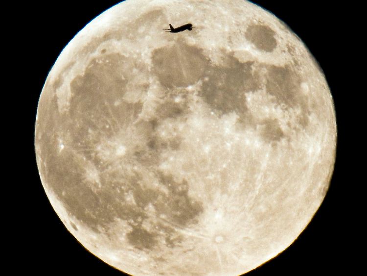 Winzig wirkt das Verkehrsflugzeug (oben im Bild), das am 26. Juni 2010 am Nachthimmel über Frankfurt am Main am Vollmond vorbeifliegt.