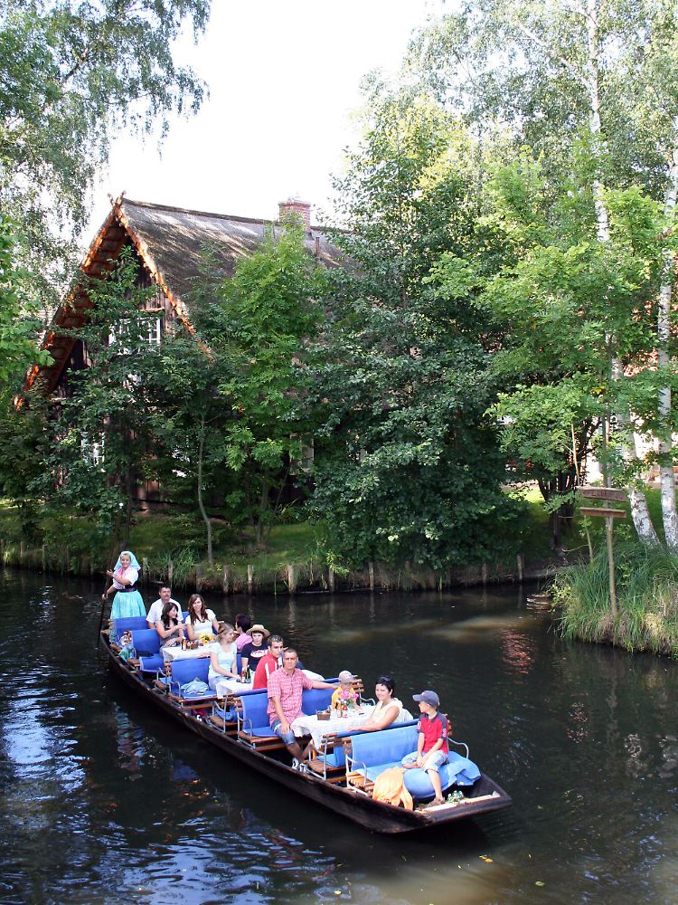 Ohne Motorkraft durch den Spreewald - im Holzkahn geht es vorbei am Ufer mit dichten grünen Büschen und urigen Häuschen.