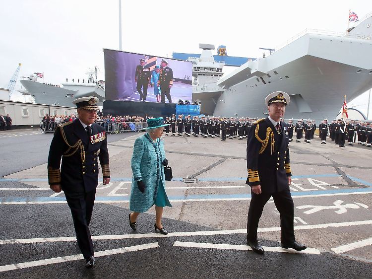 Auf dem Weg zur Taufe: Der Duke of Edinburgh, Prinz Philip (l.) und die Monarchin lassen sich von einem hochrangigen Marine-Offiziellen über die Werftanlagen in Rosyth führen.