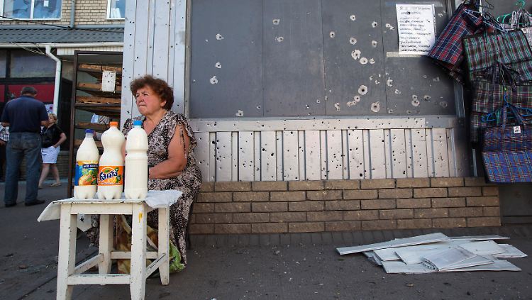 Eine Straßenverkäuferin vor einem Laden mit Schrapnell-Spuren in der ost-ukrainischen Stadt Slawjansk.