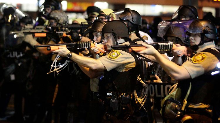 Bewaffnete Polizisten richten ihre Gewehre auf Demonstranten - eine Szene mit Symbolwert. 