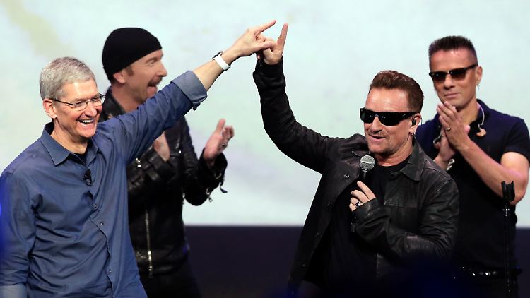 Ein Deal, von dem beide profitieren: Apple-Chef Tim Cook (l.) und U2-Sänger Bono freuen sich gemeinsam - genau wie Gitarrist The Edge (hinten links) und Schlagzeuger Larry Mullen Jr. (r.)