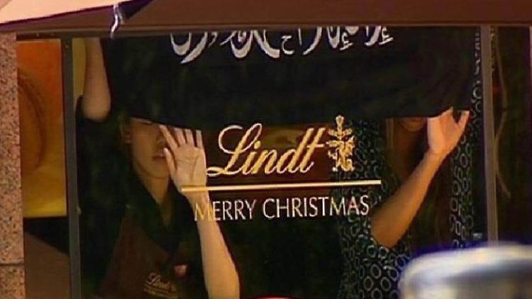 Die Geiseln werden gezwungen, eine Flagge mit arabischen Schriftzeichen hochzuhalten.