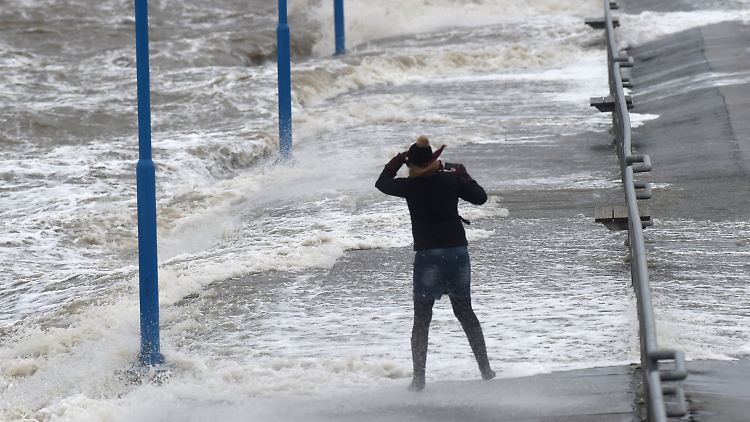 Wellen überspülen den Fähranleger in Dagebüll (Schleswig-Holstein), während eine Frau gegen den Wind kämpft.