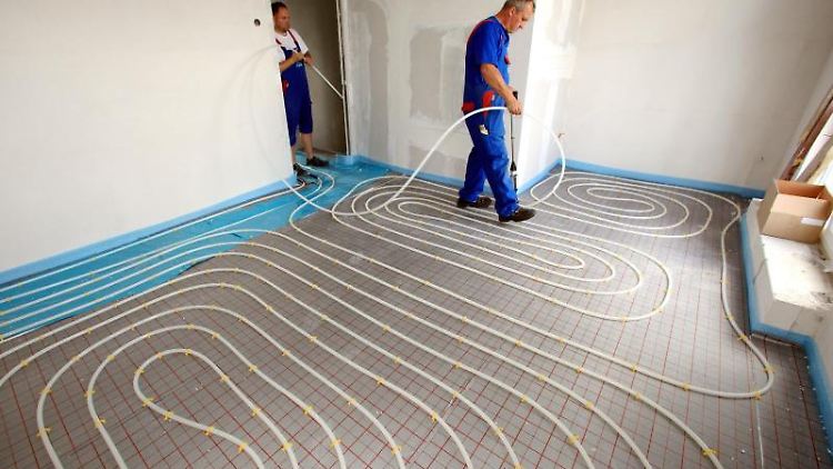 Bei der Installation einer Fußbodenheizung werden Schläuche mithilfe eines Tackers auf Dämmplatten verlegt, darüber kommt Estrich.  