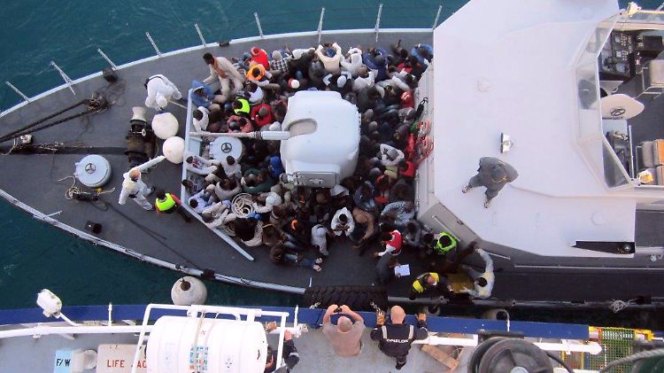 Eine Gruppe geretteter Flüchtlinge sitzt auf einem Schiff der italienischen Küstenwache.