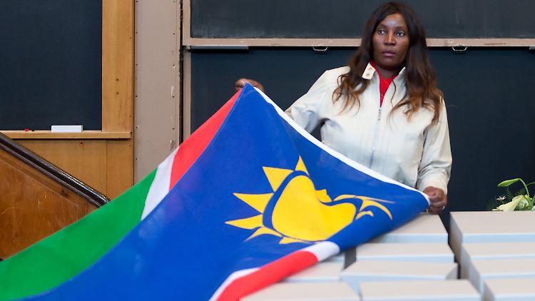 Übergabe von Gebeinen aus Namibia im März 2014. Eine Teilnehmerin der namibischen Staatsdelegation entfernt in der Berliner Charité die namibische Flagge von Behältnissen mit den sterblichen Überresten.