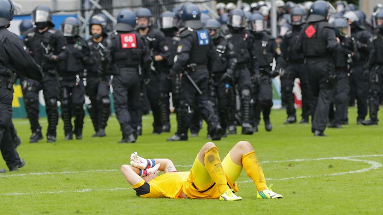 Der Offenbacher Torhüter Daniel Endres liegt nach der 1:3-Niederlage auf dem Rasen. Im Hintergrund schauen ihm die Polizisten zu, die zuvor einen Platzsturm Offenbacher Fans beendet hatten.