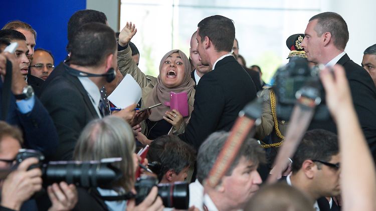 Die Frau mit dem Kopftuch ruft lautstark, "Al-Sisi ist ein Mörder!". Die ägyptische Presse-Delegation schreit sie nieder: "Es lebe Ägypten, es lebe Ägypten." Die Frau wird abgeführt, weil sie keine Ruhe gibt.