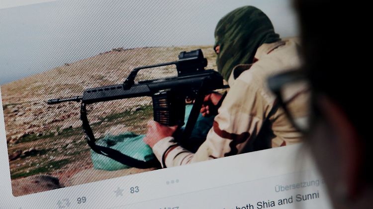 Eine Frau schaut auf einem Computer eine Internetseite mit IS-Proganda an. Der abgebildete Kämpfer hält ein möglicherweise illegal erbeutetes G36-Gewehr im Anschlag. Für welche Seite dieser kämpft, geht aus den Informationen nicht hervor.