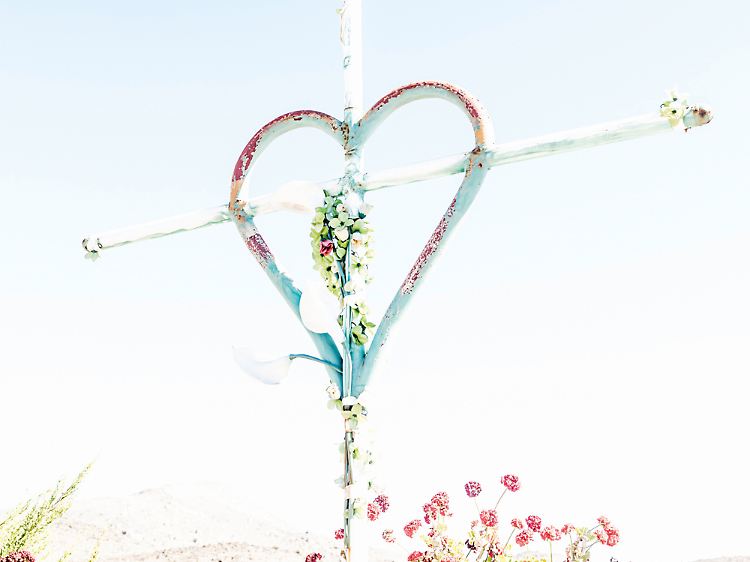 Herz aus Stahl und Blumen am Kreuz vor wolkenlosem Himmel und brennender Sonne.