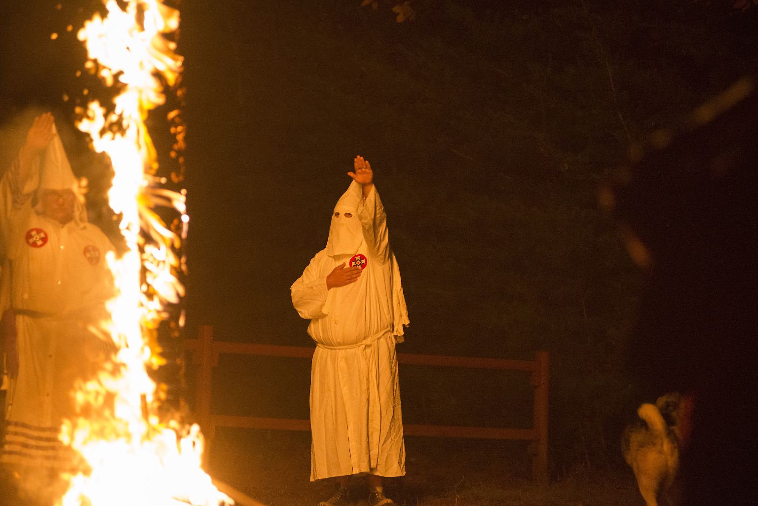 Männer in Kutten und mit Spitzkapuzen auf dem Kopf stehen an brennenden Kreuzen.
