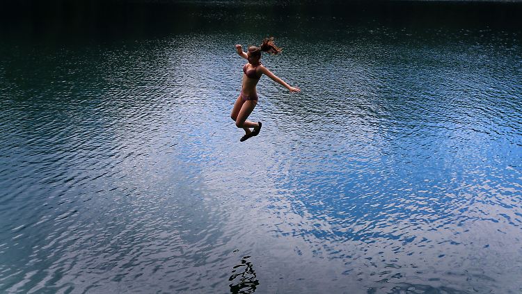 Ein junge Frau springt in den Alatsee bei Füssen.