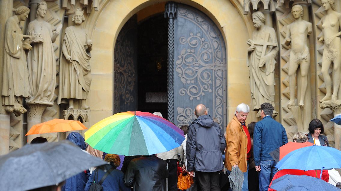 Auch ohne Sonnenschein sehenswert: Touristen mit Regenschirmen vor dem Eingang des Doms in Bamberg.
