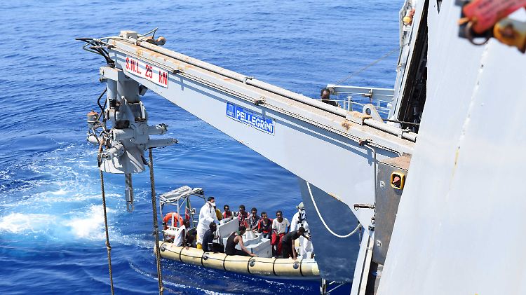 Ein italienisches Marineschiff nimmt Menschen aus einem Schlauchboot auf.