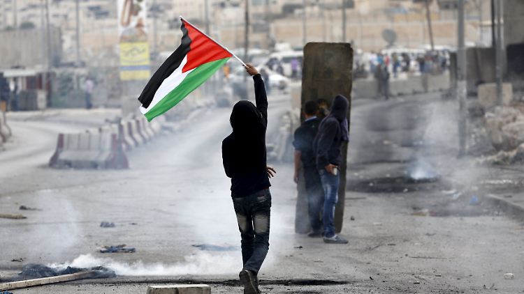 Ein palästinensischer Demonstrant hält seine Landesflagge hoch, während es mit der israelischen Arme zu Zusammenstößen kommt.