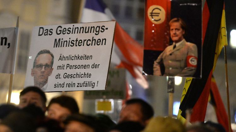 Montagabend in Dresdens Straßen: Pegida-Anhänger zeigen ein Schild mit der Aufschrift "Das Gesinnungs-Ministerchen - Ähnlichkeiten mit Personen der dt. Geschichte sind rein zufällig" und einem Bild von Bundesjustizminister Heiko Maas. Dahinter ein Bild mit Kanzlerin Merkel in einer stilisierten Nazi-Uniform.