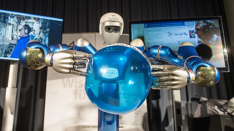 Roboter Justin balanciert bei der Präsentation des Roboterprojektes "Tele-Handshake" im DLR einen Ball in den Händen. Gesteuert wird er vom Kosmonauten Sergei Wolkow auf der ISS, der die linke Hand bewegt (linker Monitor) und einem Wissenschaftler in St. Petersburg, der die rechte Hand steuert (rechter Monitor).